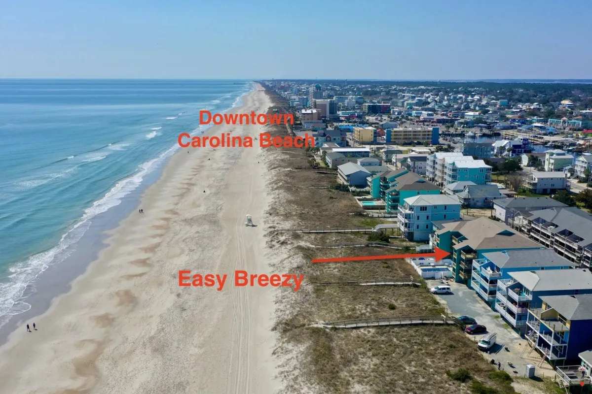 A sweeping exterior view of Easy Breezy’s beachfront setting, capturing the sandy shoreline, ocean waves, the property itself, and glimpses of the nearby downtown area. The tranquil beach is inviting for morning walks or sunset strolls, and the ocean waves set a romantic, relaxing scene.