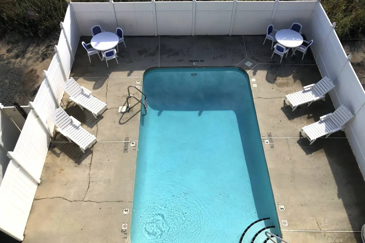 A sparkling swimming pool bordered by lounge chairs and a table with seating, inviting guests to swim, sunbathe, or socialize. The leisurely atmosphere is enhanced by sunlight and a clear, spacious pool deck.