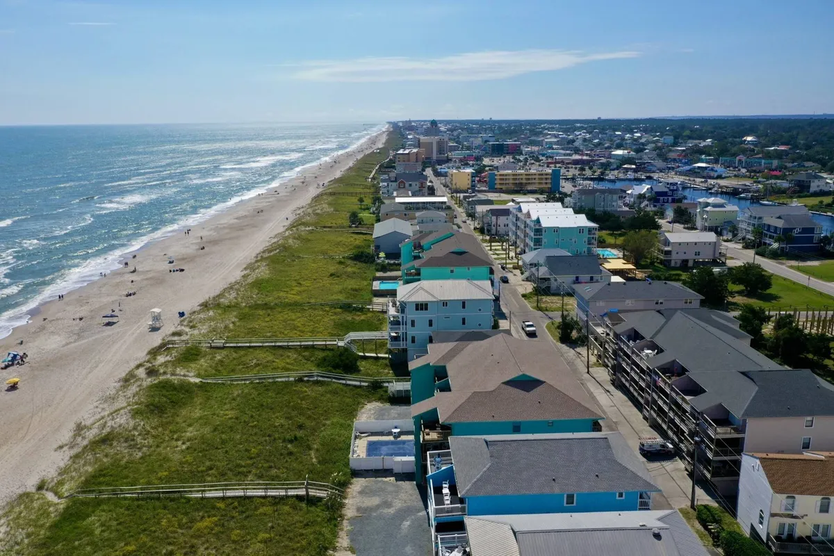 A lively beachfront scene with ocean waves, colorful houses, and the bustling boardwalk in the background. People can be seen walking along the beach, participating in various activities, and exploring nearby shops and restaurants.