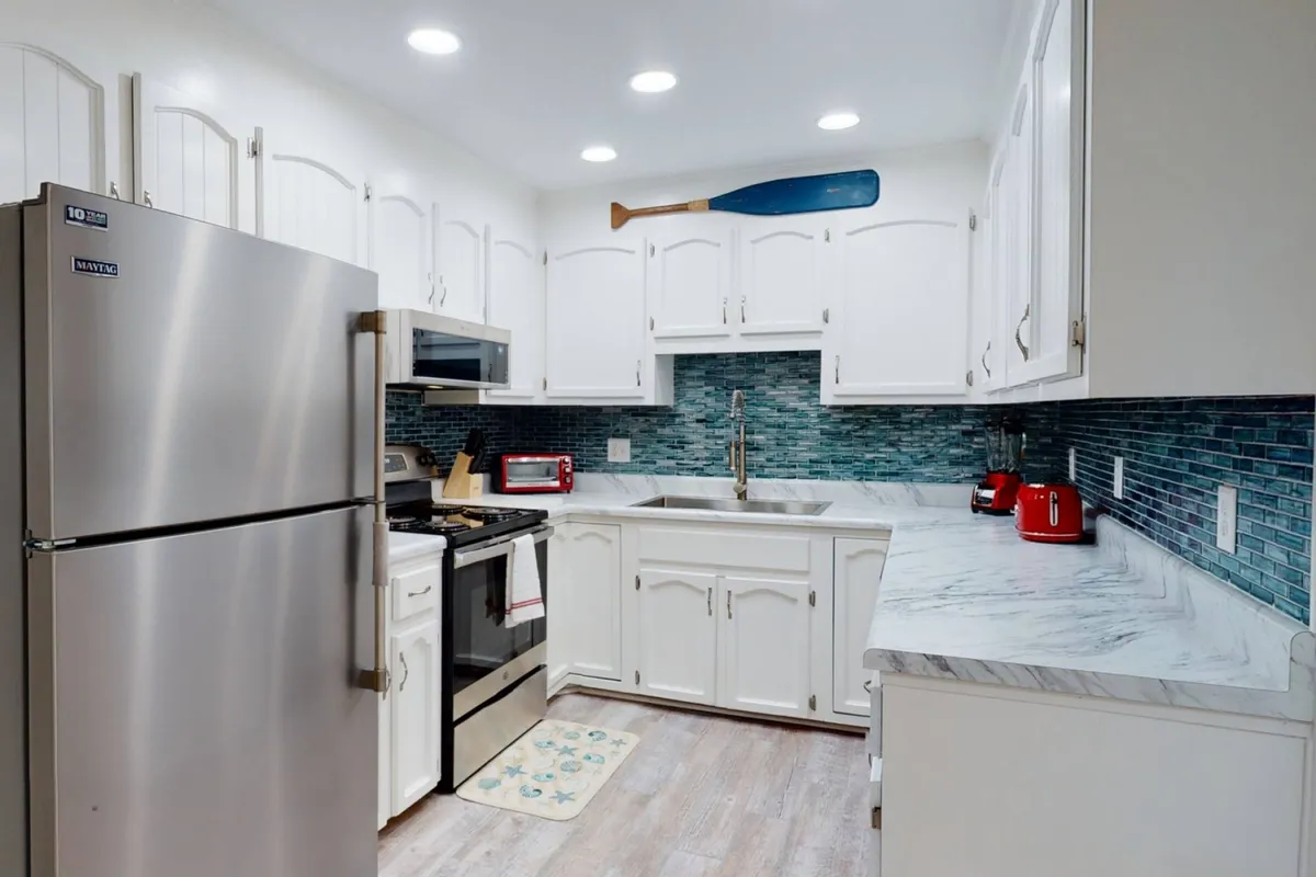 A bright and modern kitchen with a stainless steel refrigerator, vibrant blue backsplash, and a full array of appliances. The layout is open to the rest of the living space, encouraging socializing while preparing food.
